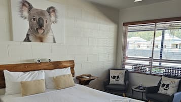 Een hotelkamer met een groot bed, een plafondventilator, een raam met uitzicht en een schilderij van een koala aan de muur.