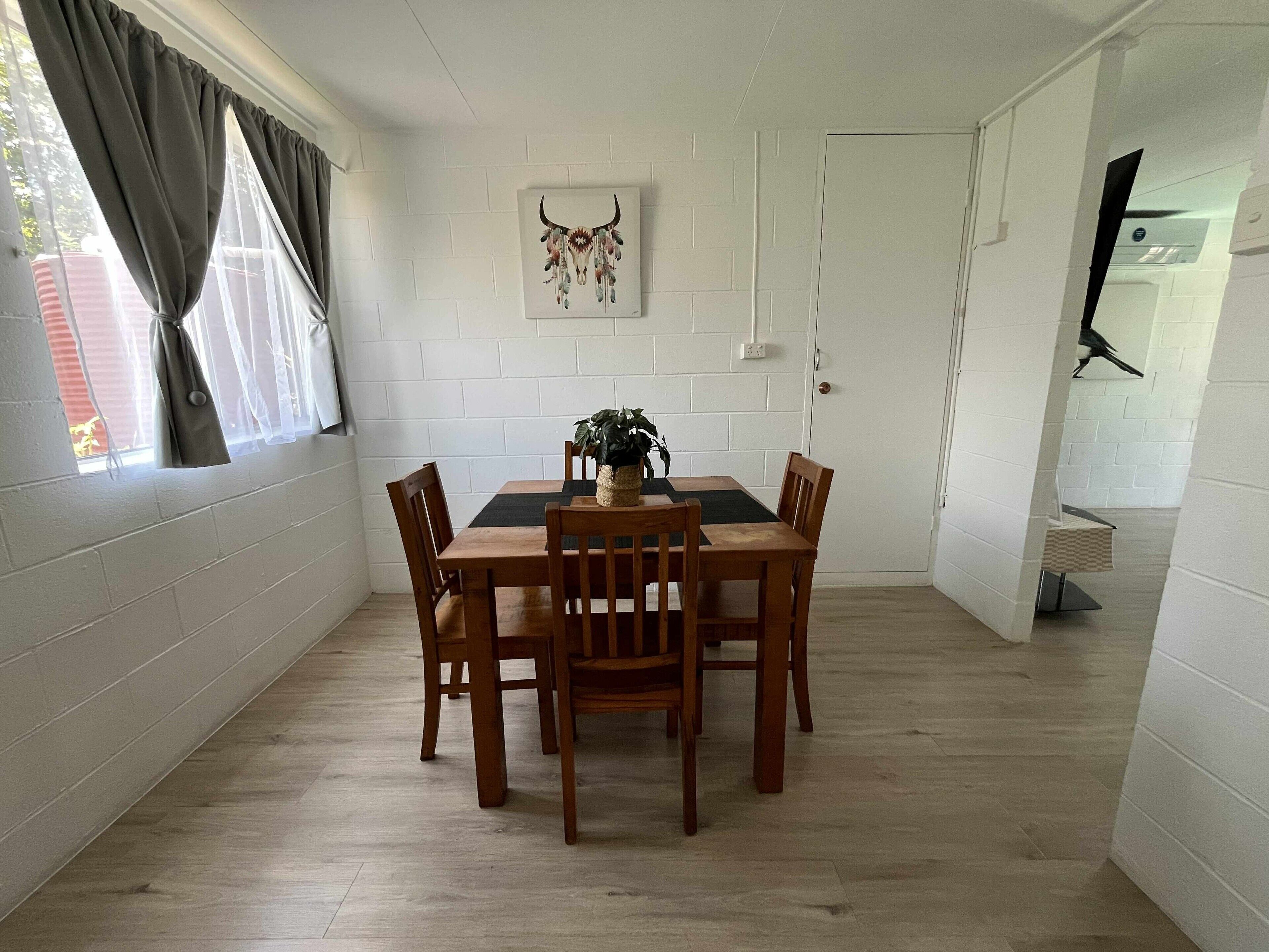 A dining area with a wooden table and chairs, a potted plant, and a wall-mounted artwork.