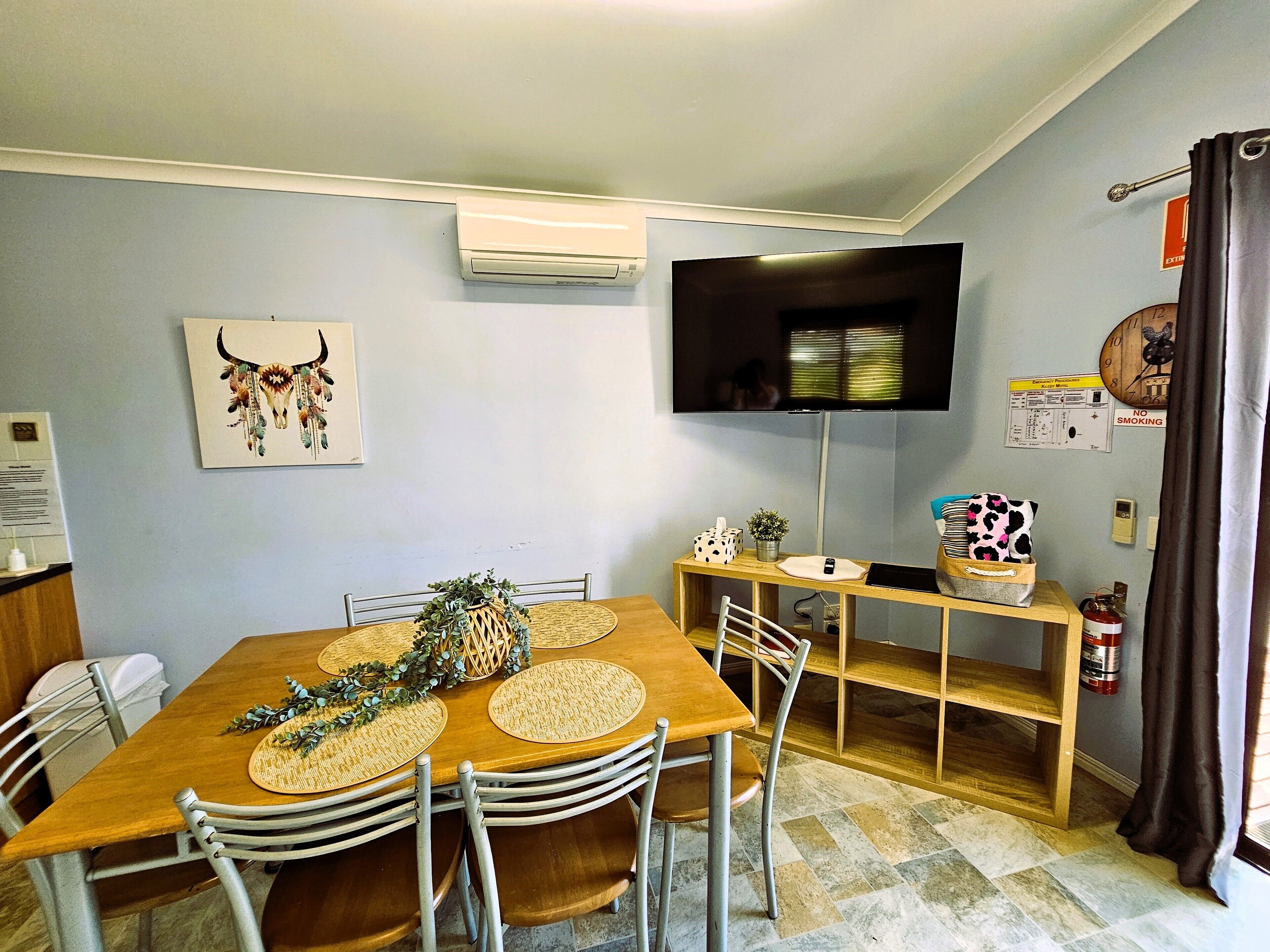A dining area with a wooden table, metal chairs, a mounted flat-screen TV, and a wall-mounted air conditioner.