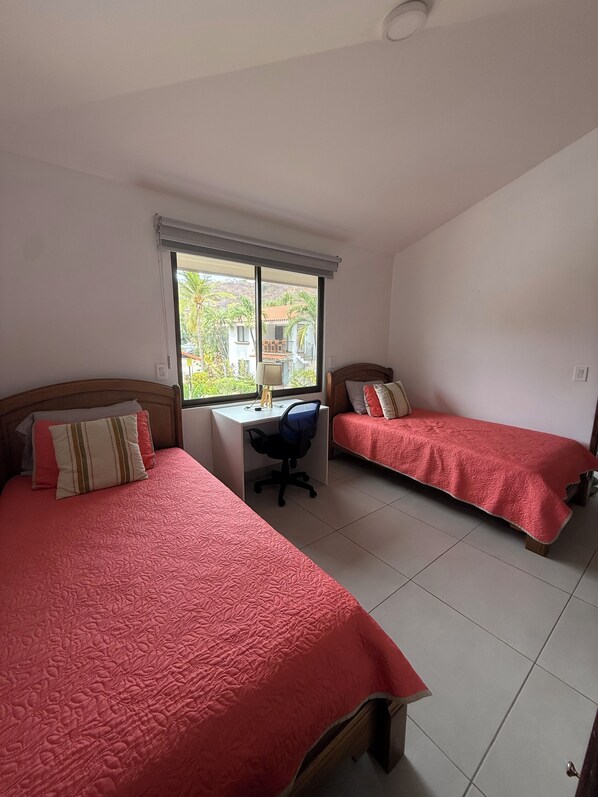 A room with two beds, a desk, and a window with a view of buildings and trees. - Amazing Condo! Playas del Coco (Provincia de Guanacaste)