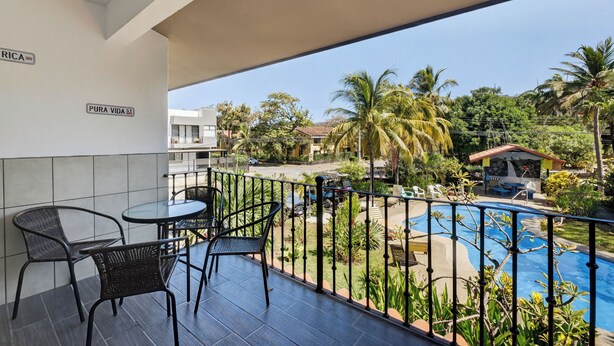 A balcony with a pool view, outdoor seating, and a sign that reads 'PURA VIDA.' - Amazing Condo! Playas del Coco (Provincia de Guanacaste)