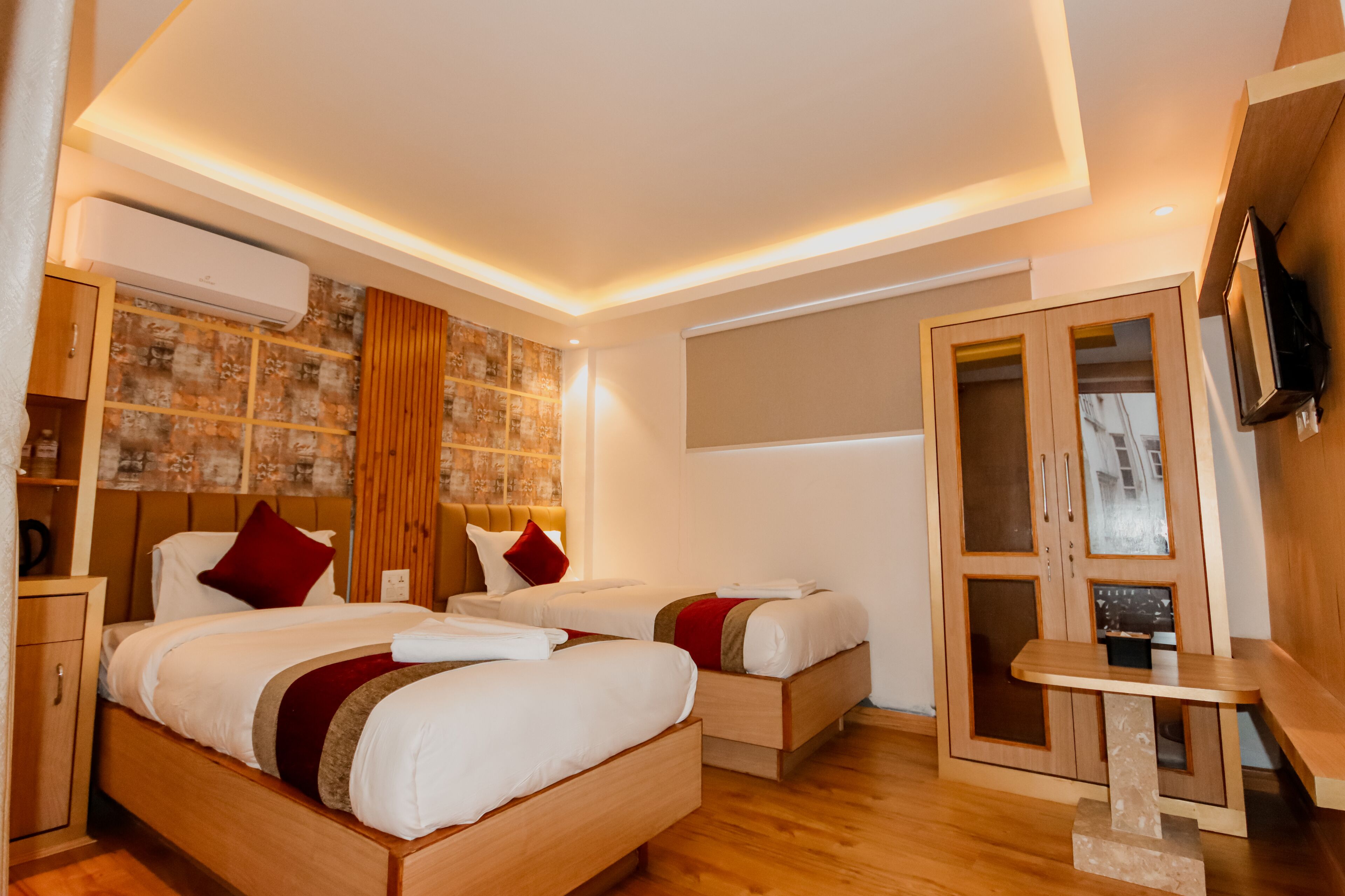 Una camera d'albergo moderna con due letti, un armadietto in legno, una TV e un tavolino.