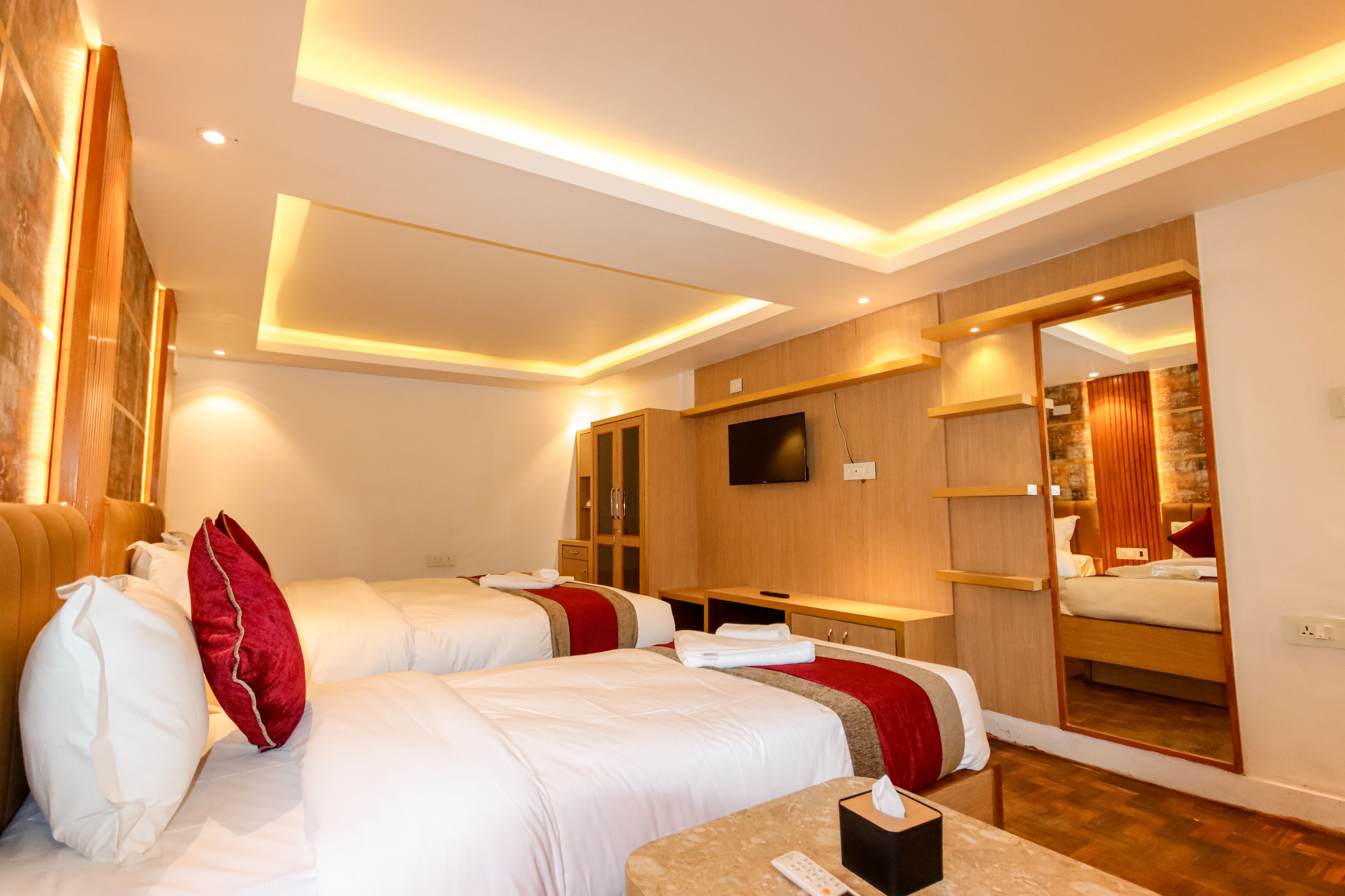 A hotel room with two beds, a TV, a mirror, and a wooden wardrobe.