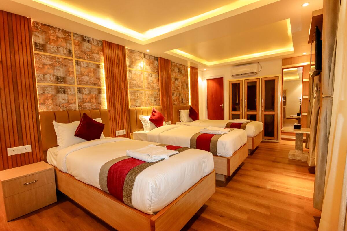 A hotel room with two beds, wooden flooring, and a large window with curtains.