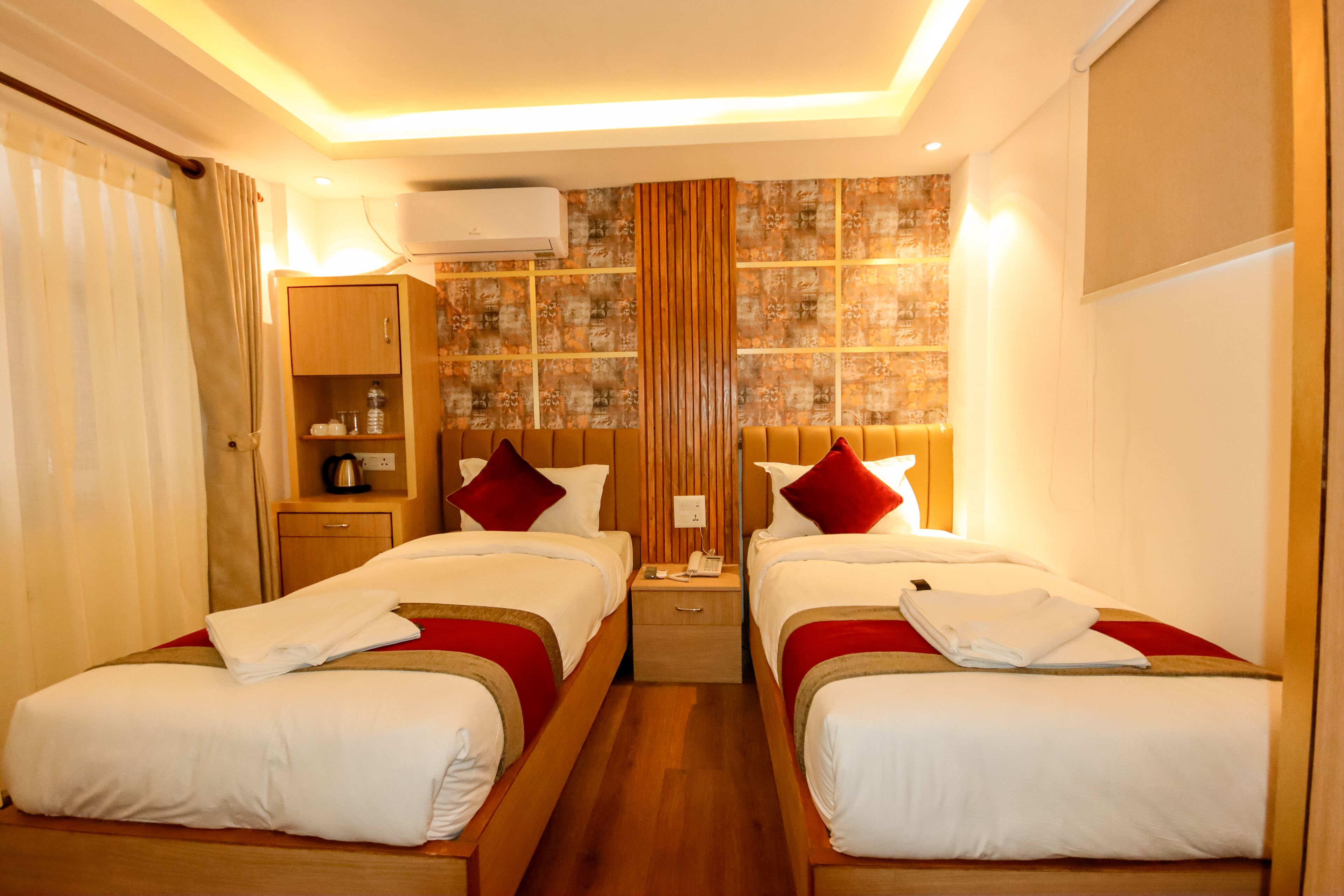 A hotel room with two beds, a wardrobe, a nightstand, and an air conditioning unit.