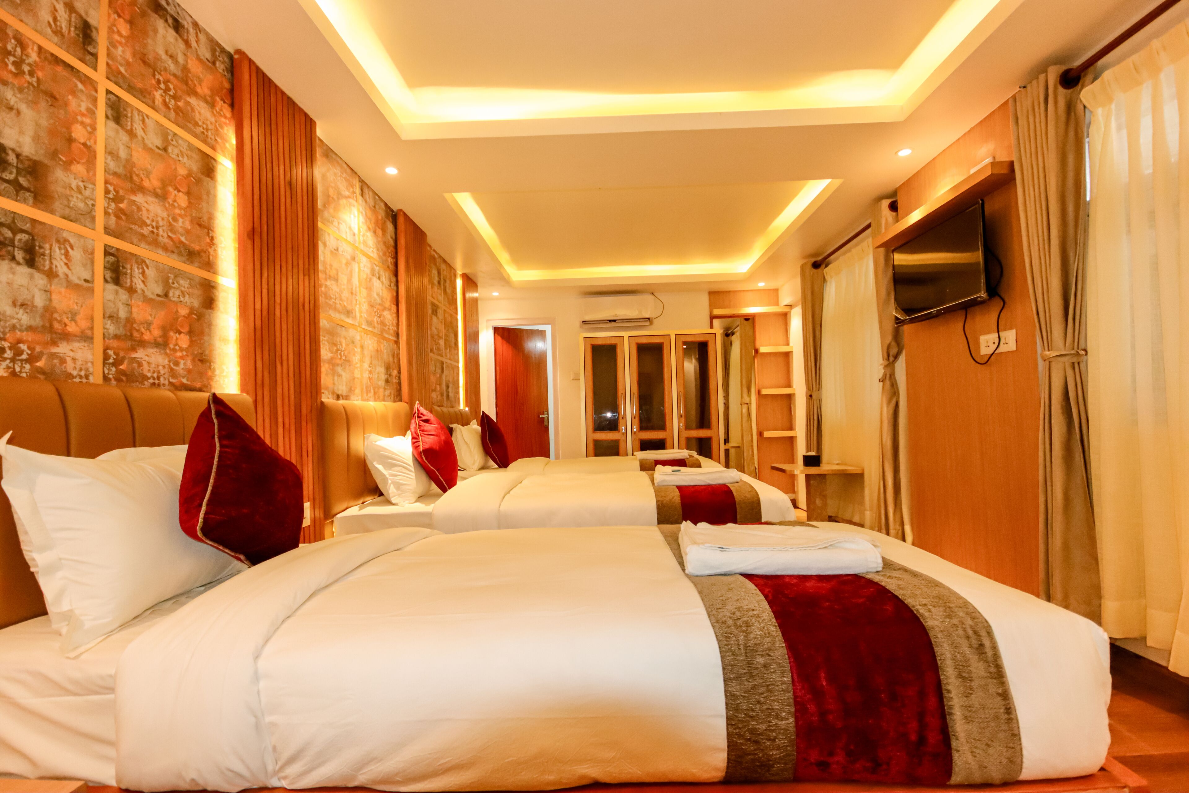Habitación de hotel con dos camas, televisor, espejo y pared de madera.