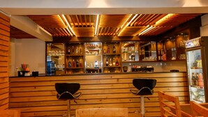 Una zona de bar con listones de madera en el techo, taburetes y estanterías llenas de botellas.