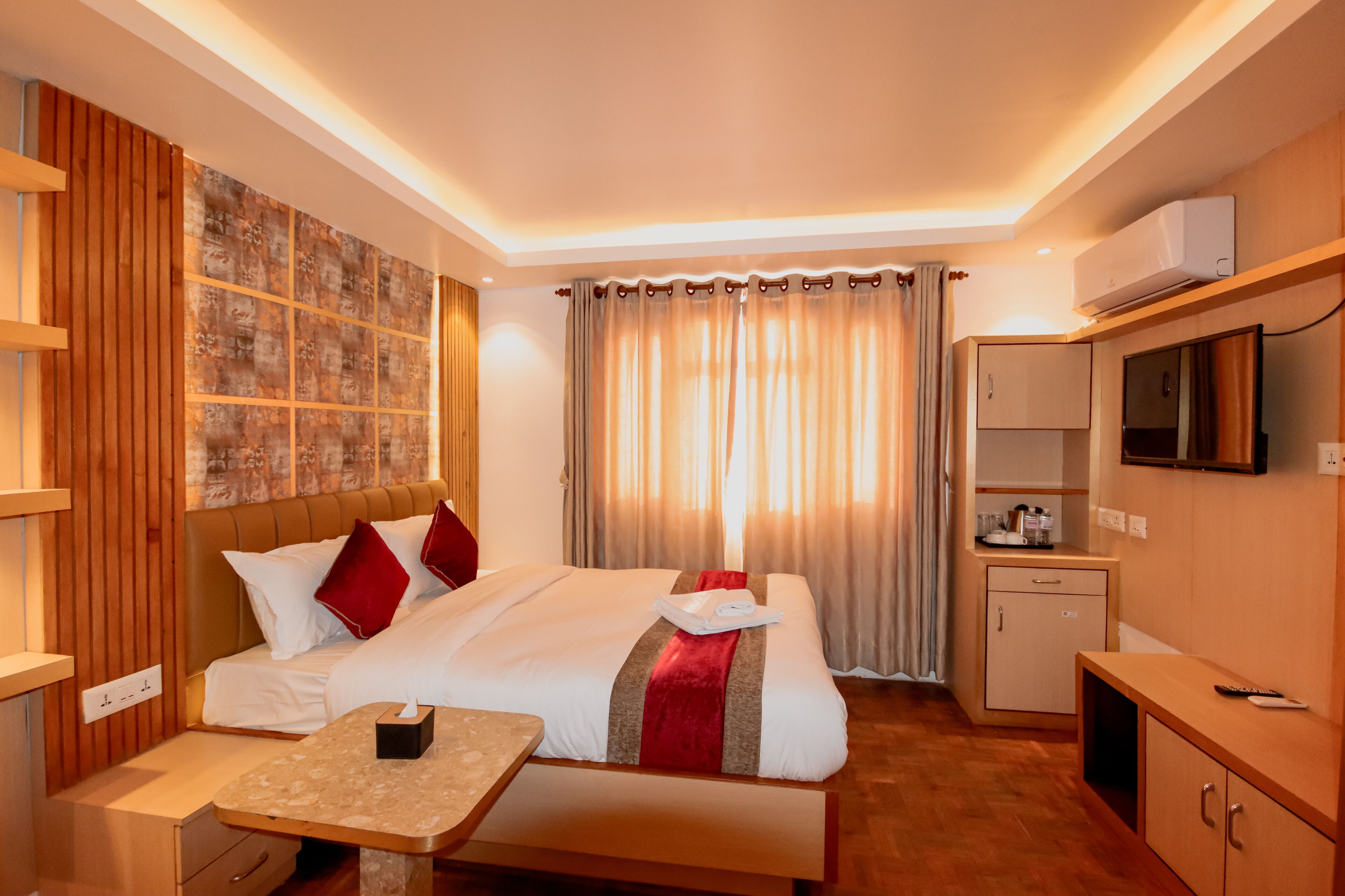 A hotel room with a bed, bedside table, TV, and a small kitchenette.
