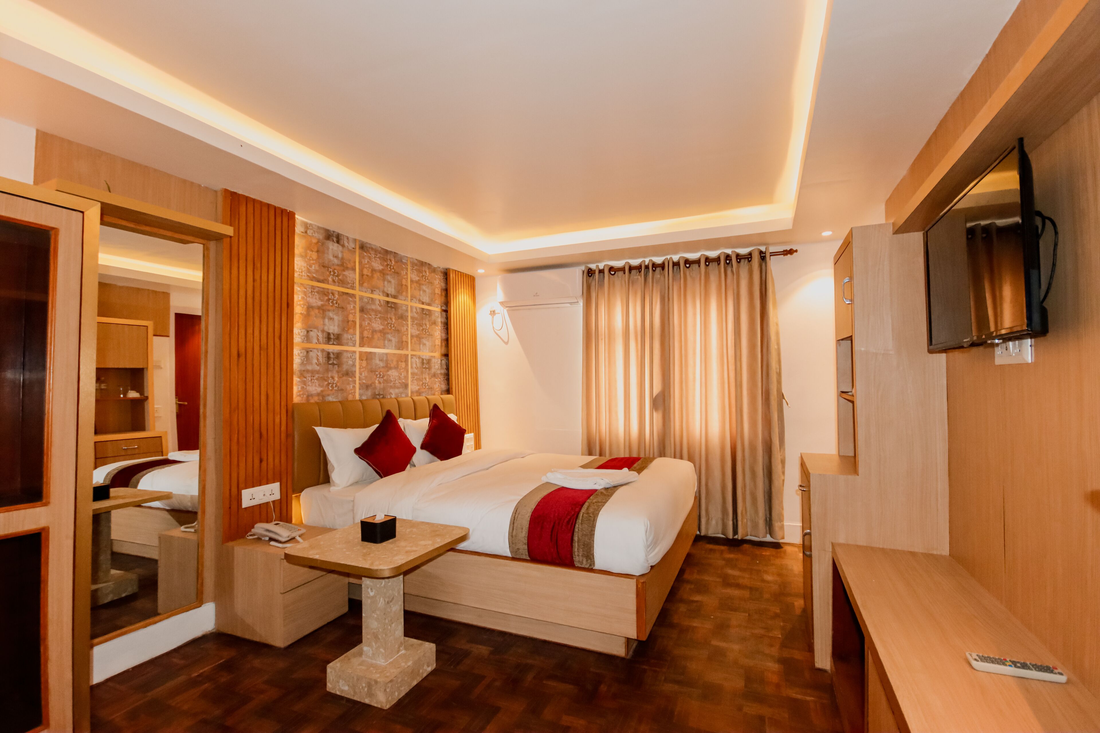 A modern hotel room with a large bed, bedside table, TV, and a mirror.