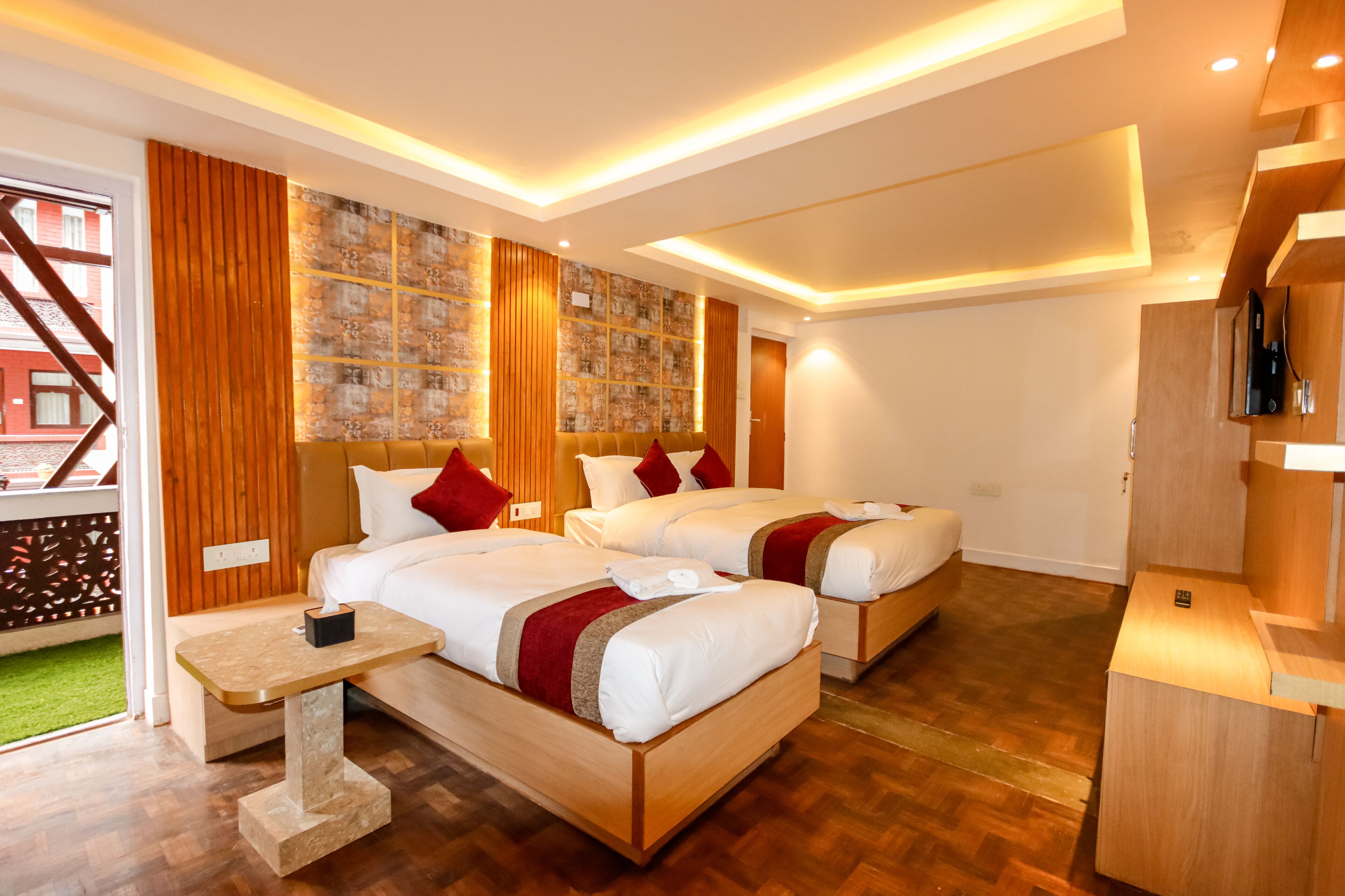 A hotel room with two beds, wooden flooring, a small table, and a wall with a patterned design.