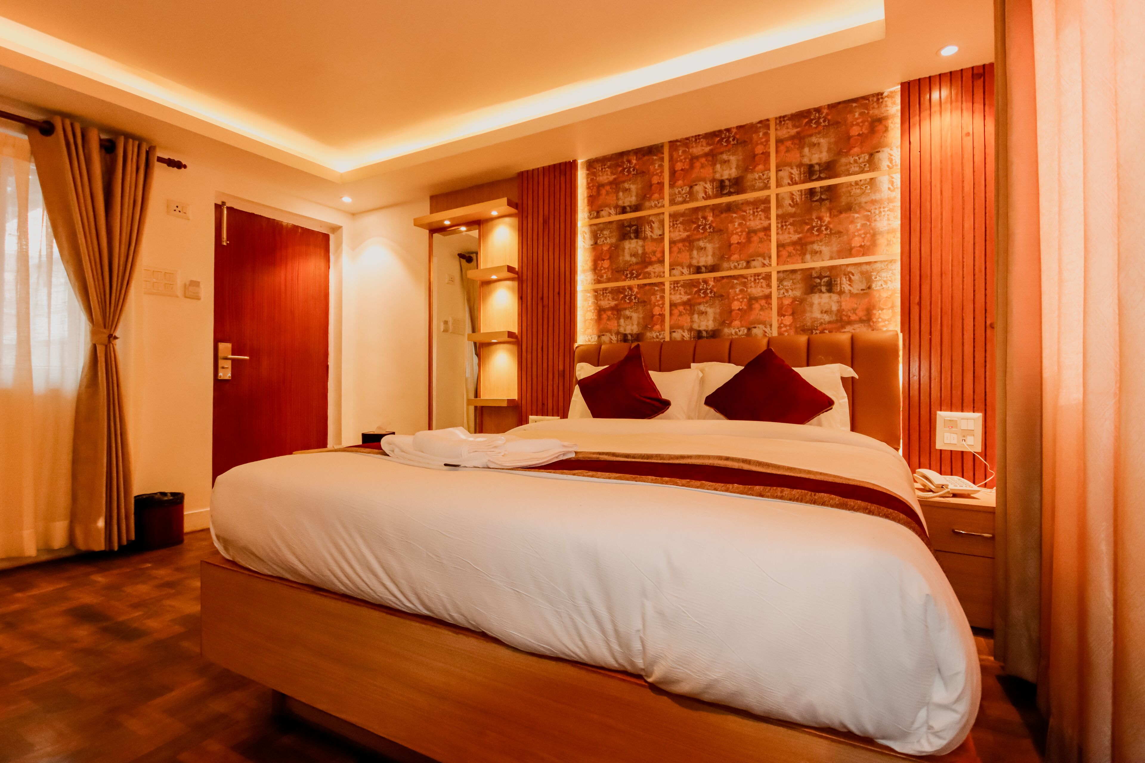 A hotel room with a large bed, wooden headboard, and a wall with a patterned design.
