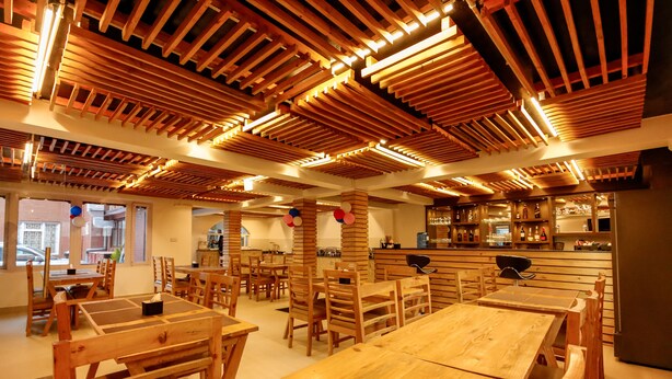 Un restaurante con mesas y sillas de madera, una zona de bar y vistas a la calle.