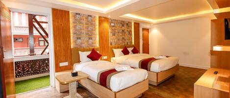 A hotel room with two beds, wooden flooring, a small table, and a view of a building outside.