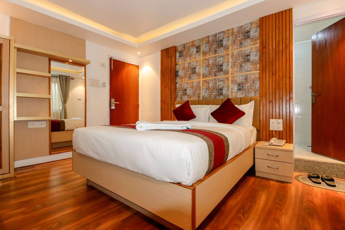 A hotel room with a large bed, a bedside table with a phone, a mirror, and a wardrobe.