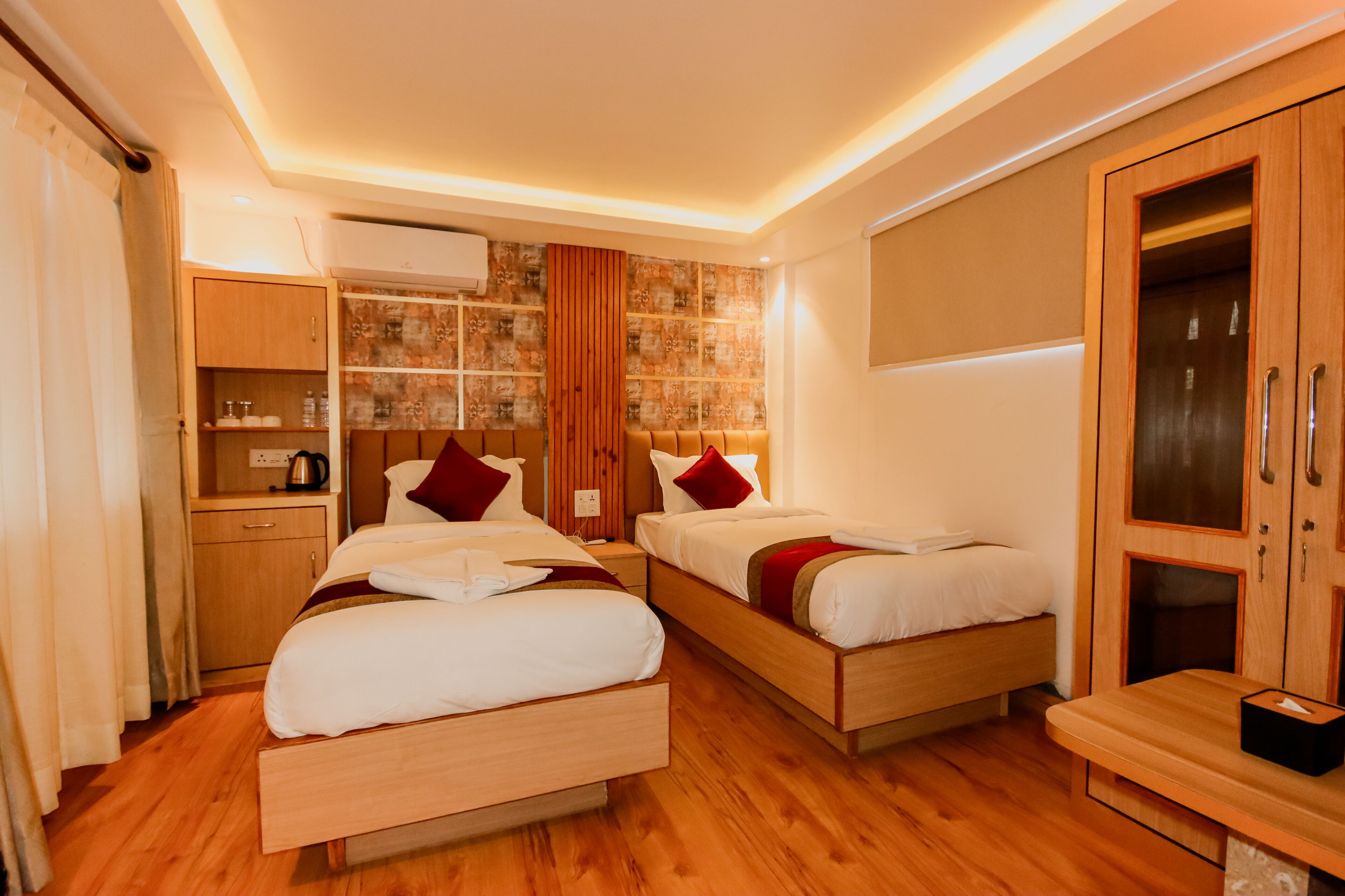 Une chambre d’hôtel avec deux lits, un plancher en bois, une armoire, un bureau avec une chaise et un téléviseur fixé au mur.