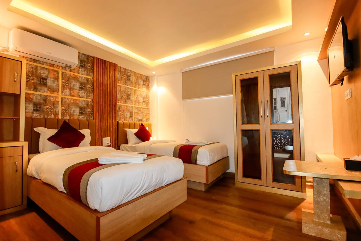 A hotel room with two beds, wooden headboards, a built-in wardrobe, and a flat-screen TV.