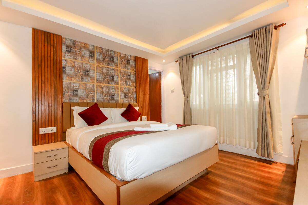 A modern hotel room with a large bed, wooden panel wall, and a large window with curtains.