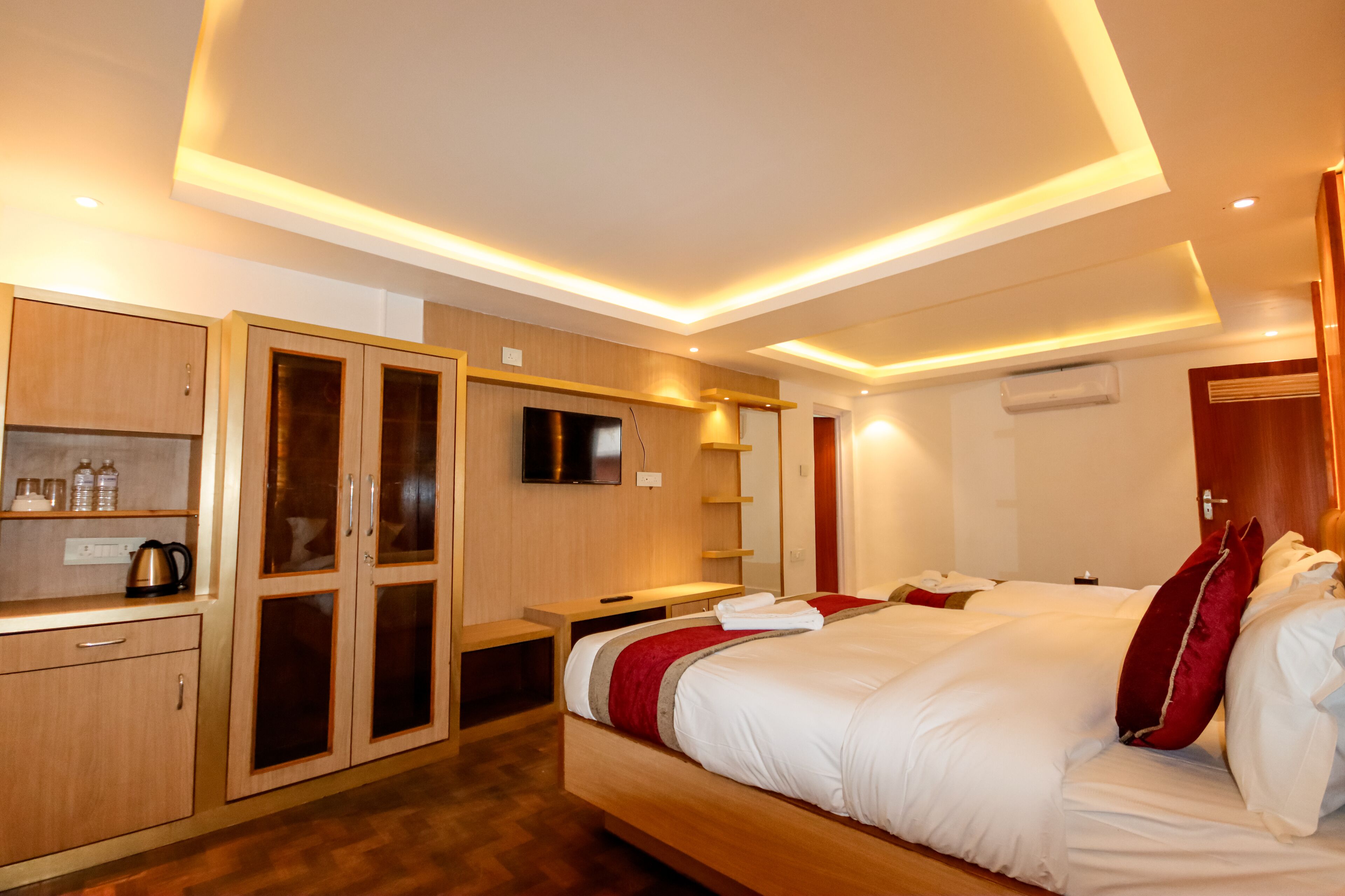 A modern hotel room with a large bed, wooden wardrobe, bedside tables, and built-in TV.