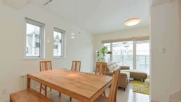 A modern living room with a wooden dining table and chairs, a sofa, and a large window providing a view of the city. - S12 HOTEL (Sapporo)