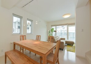 Sala moderna com mesa de jantar e cadeiras de madeira, um sofá e uma janela grande com vista para a cidade.