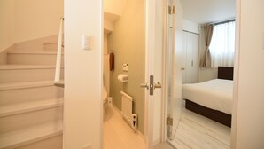 A bedroom with a bed, a bathroom with a toilet and a radiator, and a staircase leading to an upper floor. - S12 HOTEL (Sapporo)