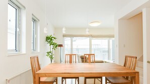 A spacious dining area with a large wooden table and six chairs, large windows with blinds, and a potted plant. - S12 HOTEL (Sapporo)
