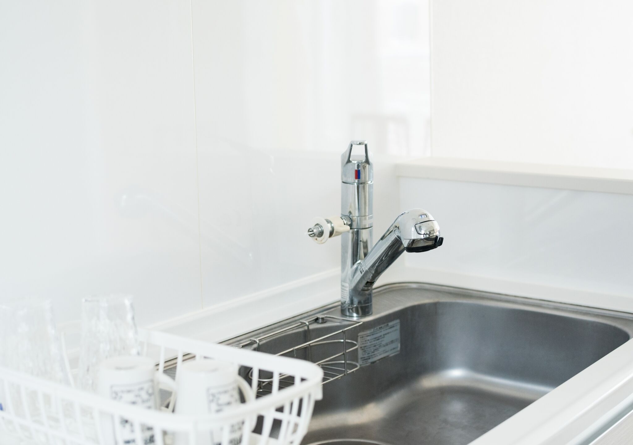 A stainless steel kitchen sink with a modern faucet, a white dish rack with glasses, and a white backsplash.