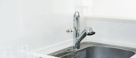 A stainless steel kitchen sink with a modern faucet, a white dish rack with glasses, and a white backsplash.