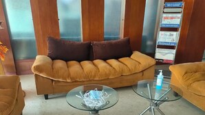 Una sala de estar moderna con un sofá marrón, dos mesas de centro de vidrio y un mueble para revistas con diversas publicaciones.