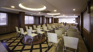 Un salón de conferencias con filas de sillas, una pantalla de proyector y un ventanal grande.