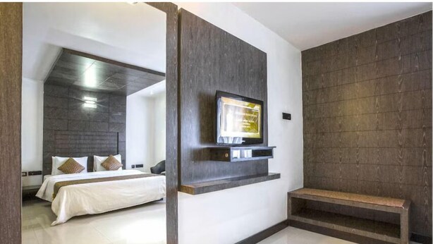 Una habitación de hotel moderna con una cama grande, un televisor montado y un banco empotrado.