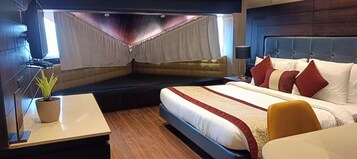 Una habitación de hotel moderna con una cama grande, una mesita de noche, un escritorio pequeño, una planta en maceta y una ventana con cortinas.