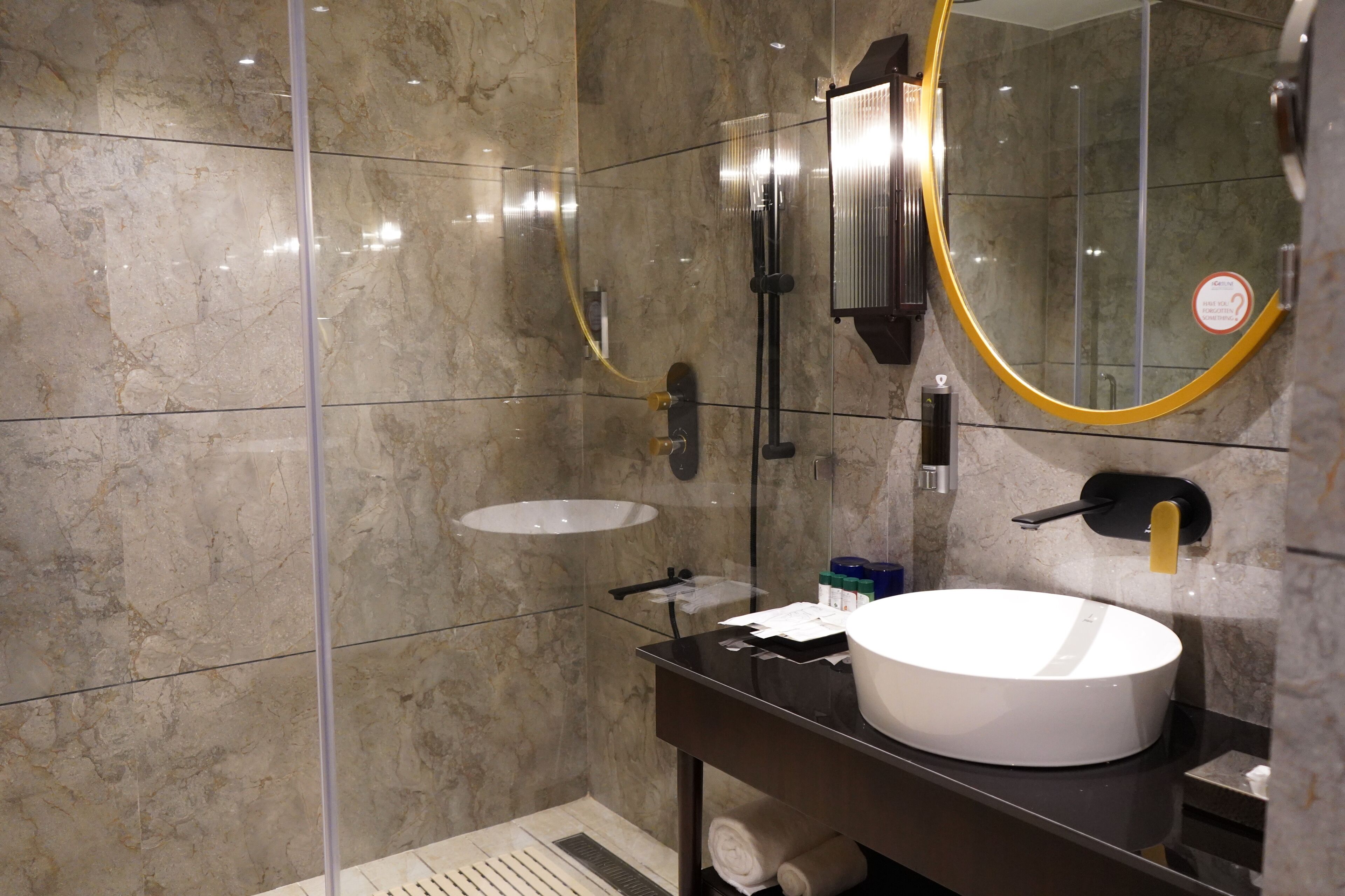 Un bagno moderno con cabina doccia in vetro, un lavabo bianco e un grande specchio con cornice dorata.