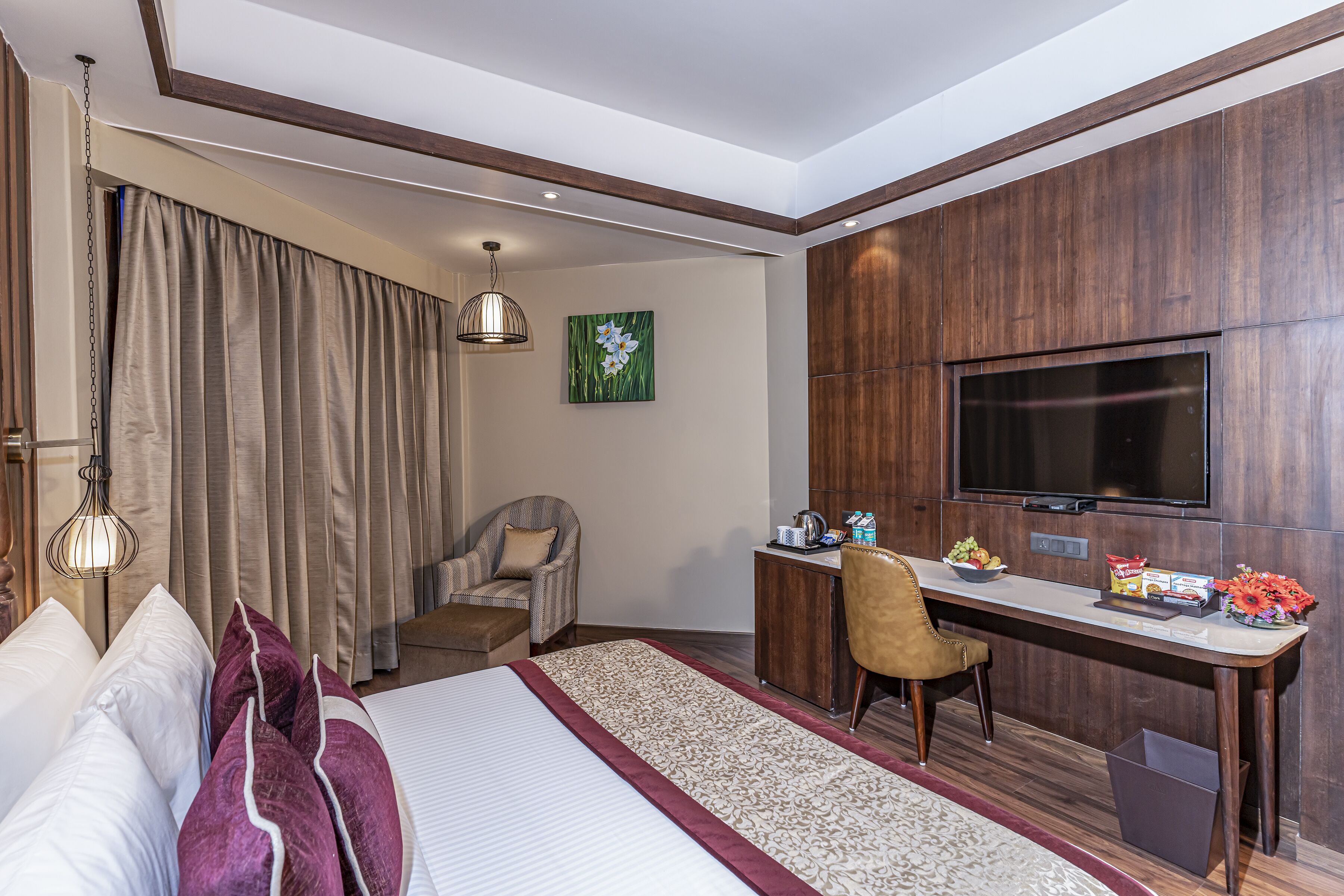 Une chambre d’hôtel équipée d’un lit, d’un bureau, d’une chaise, d’une télévision et d’une petite table sur laquelle sont disposés des en-cas et des fleurs.