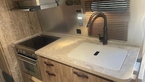 A compact kitchen with a stove, sink, and wooden cabinets. - Affordable Rare Tommy bahama skeeps 2+ in half moon bay (Mill Valley)