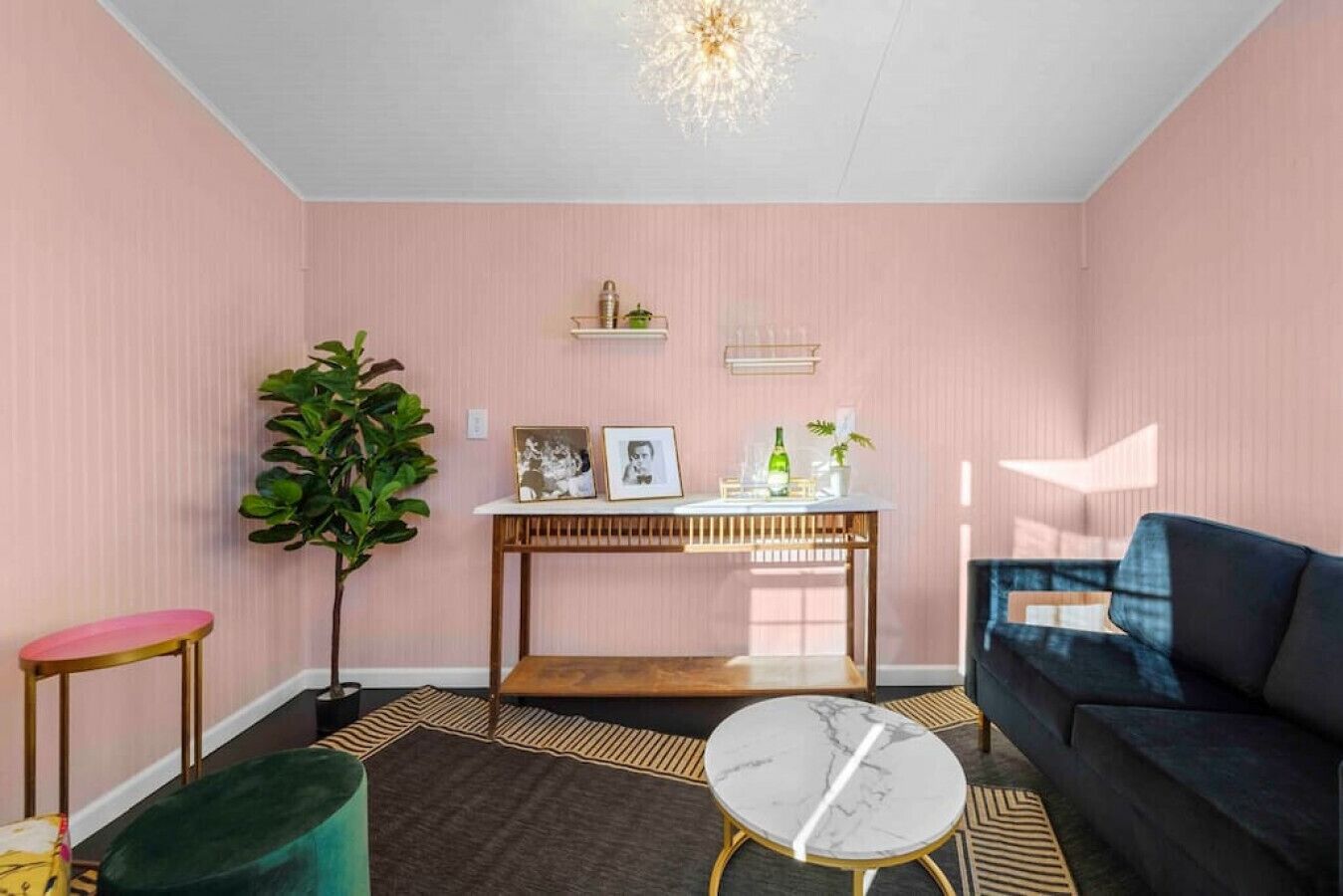 Un salon avec un mur rose, une table basse en bois, un canapé bleu, un pouf vert et une plante en pot.