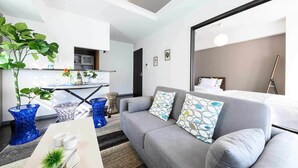 Un salon moderne avec un canapé gris, des coussins à motifs bleus et blancs, une table à manger agrémentée d’un vase et de verres, et une plante.