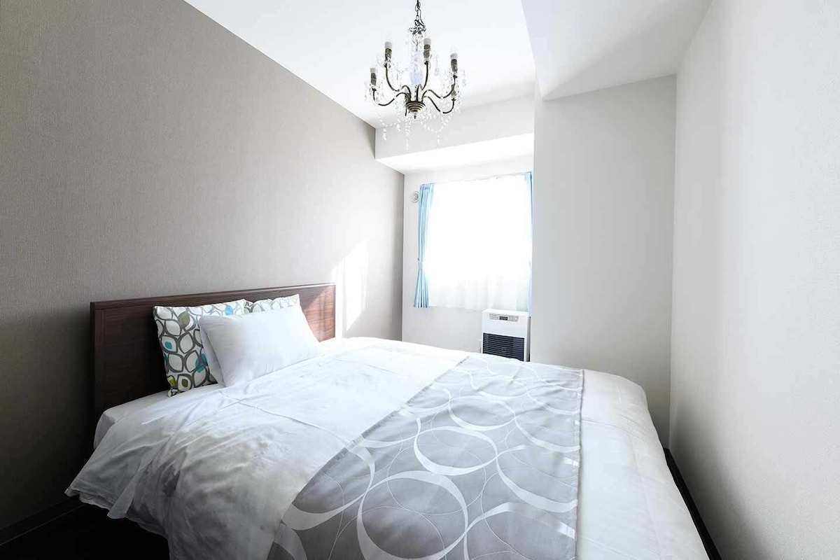 Une chambre d’hôtel avec un lit, un lustre, une fenêtre avec des rideaux et un appareil de climatisation.
