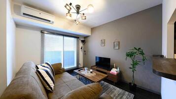 Uma sala de estar com um sofá, uma televisão, uma mesa de centro e uma planta.