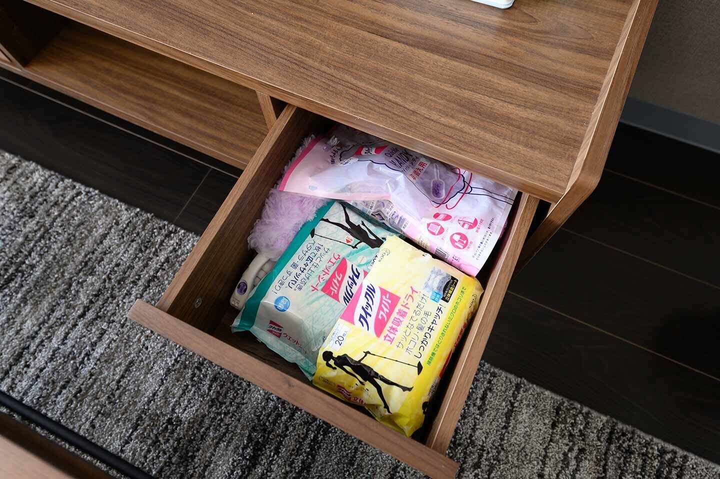 Un cassetto sotto una scrivania di legno contiene diversi oggetti, tra cui un pacco giallo, un pacco rosa e alcuni articoli bianchi.
