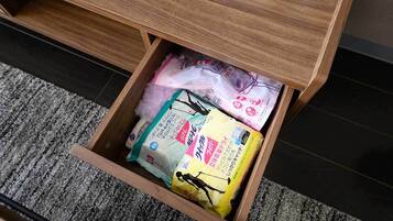 Un cassetto sotto una scrivania di legno contiene diversi oggetti, tra cui un pacco giallo, un pacco rosa e alcuni articoli bianchi.