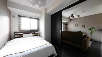 A modern bedroom with a large bed, a dark-toned sofa, and a ceiling light fixture.
