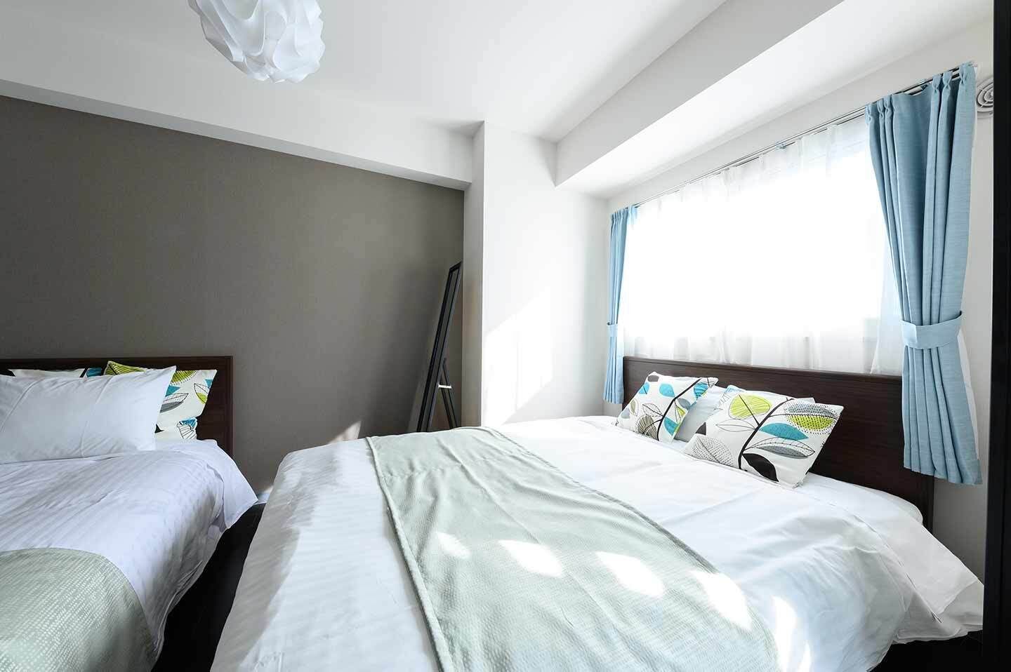 A hotel room with two beds, a large window with curtains, and a ceiling light fixture.