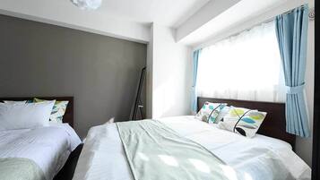 A hotel room with two beds, a large window with curtains, and a ceiling light fixture.