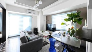 Un salon moderne avec un canapé gris, un téléviseur, une table à manger et une grande plante.