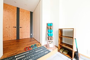 A room with wooden flooring, a shoe rack with multiple pairs of shoes, a wooden shelf unit, and a mat with text.