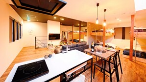 Una cocina moderna con estufa integrada, comedor con mesa y sillas de madera, literas y sala de estar con sofá y televisor.