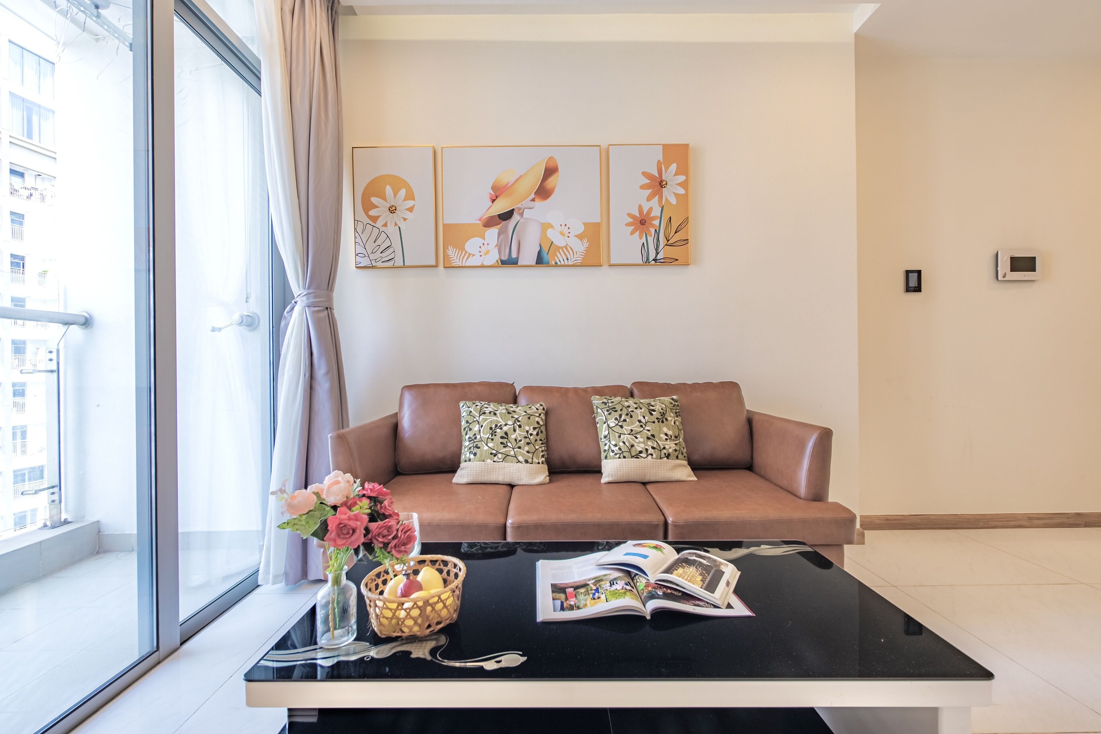 A living room with a brown sofa, two patterned cushions, a black coffee table with a magazine and a vase of flowers.