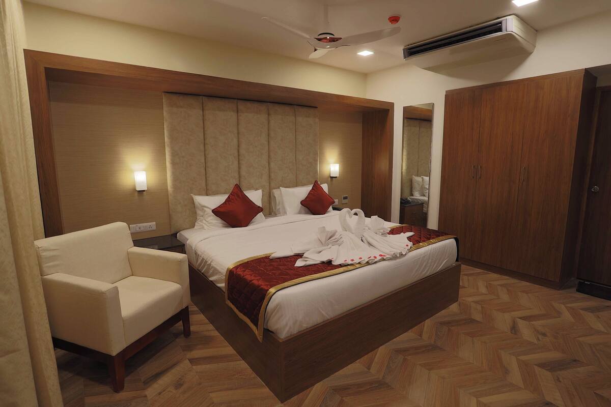 A hotel room with a large bed, a chair, a wardrobe, and a ceiling fan.