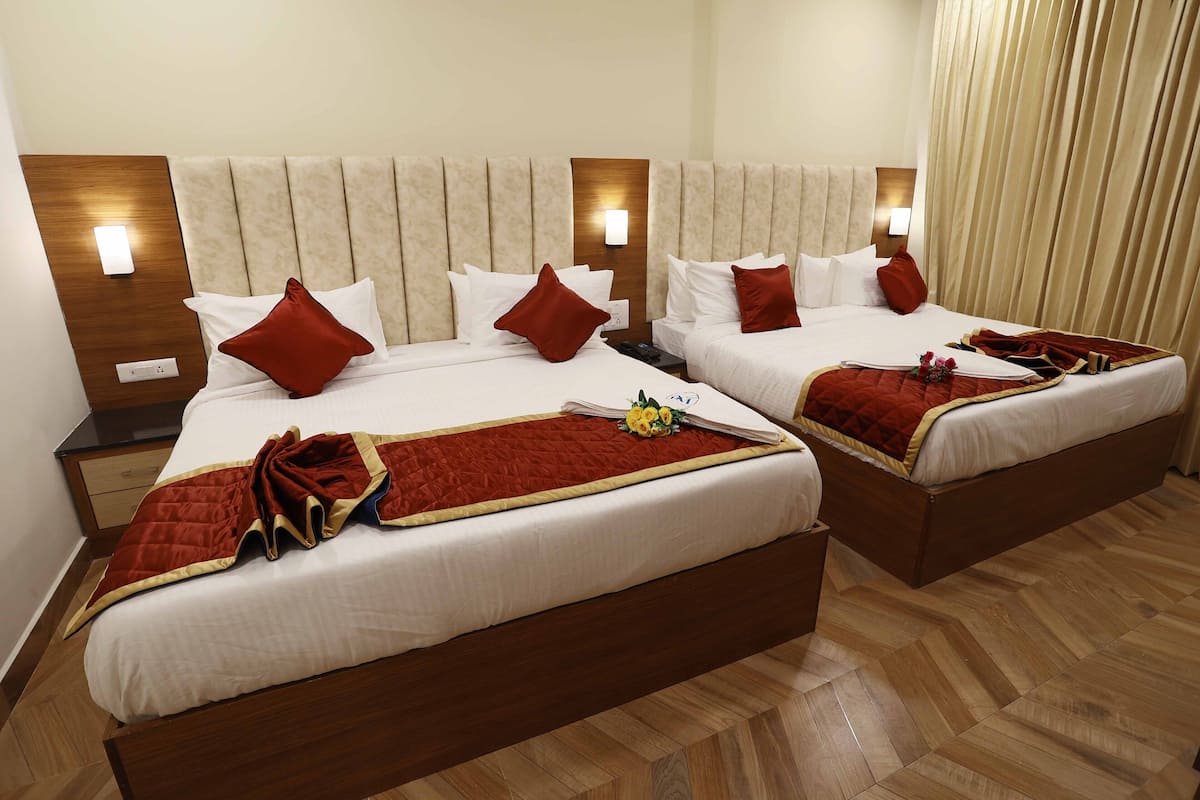 A hotel room with two beds, each with a wooden headboard, white bedding, and red throw pillows. There are bedside tables with lamps and a wooden floor.